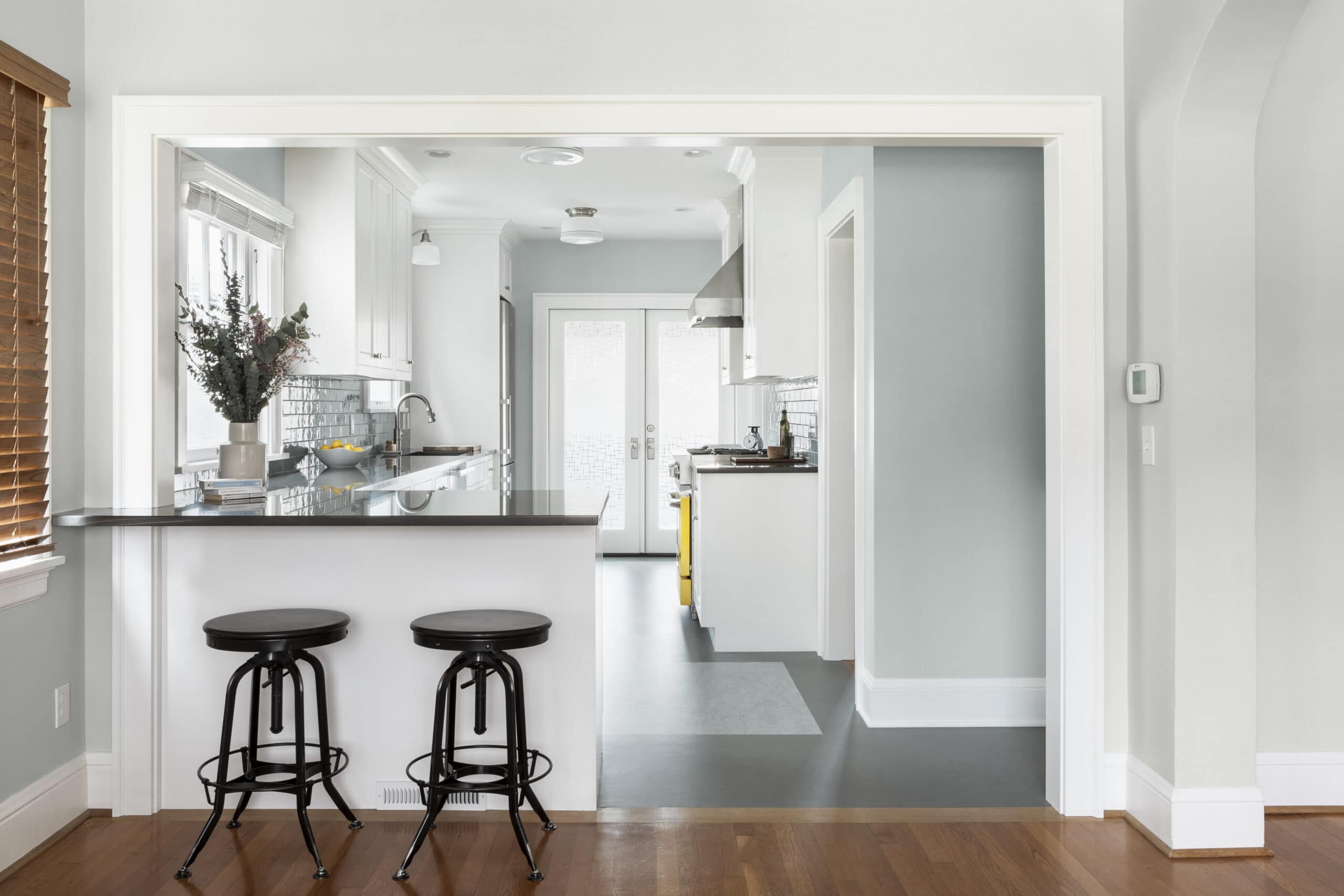 Craftsman style kitchen with white cabinets, dark countertops, marmoleum floors, with blue tile and wall color and peninsula seating