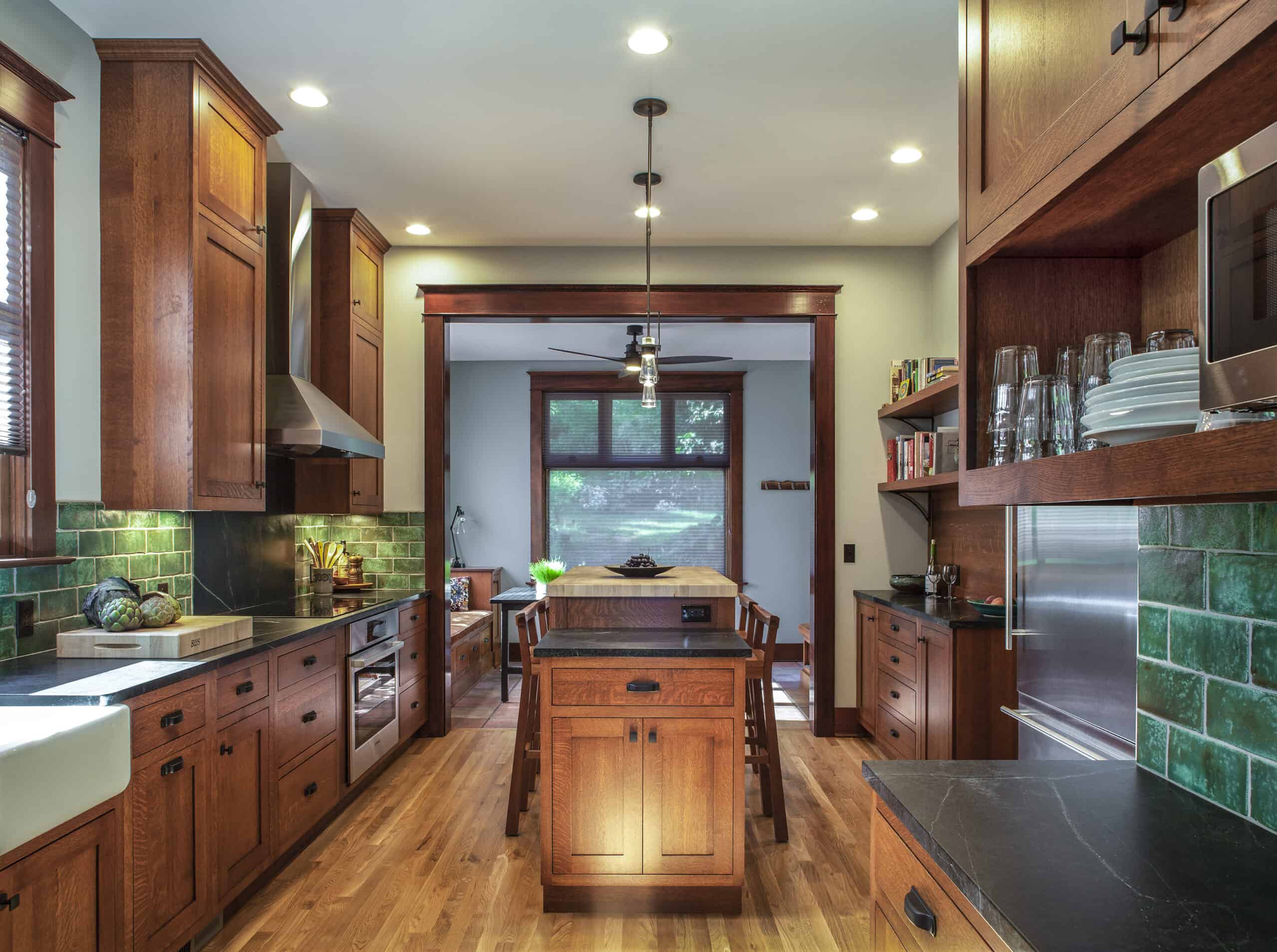 Craftsman style galley kitchen with wood cabinets, dark countertops, green tile, with an island and wood trim